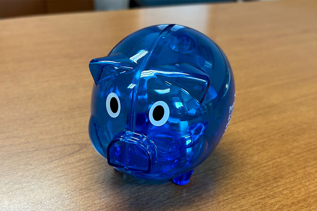 Blue, plastic, transparent piggy bank on wood table.