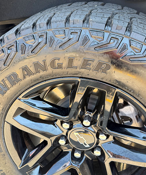 A closeup of a truck tire and wheel. The tire brand is Wrangler and the wheel is black.